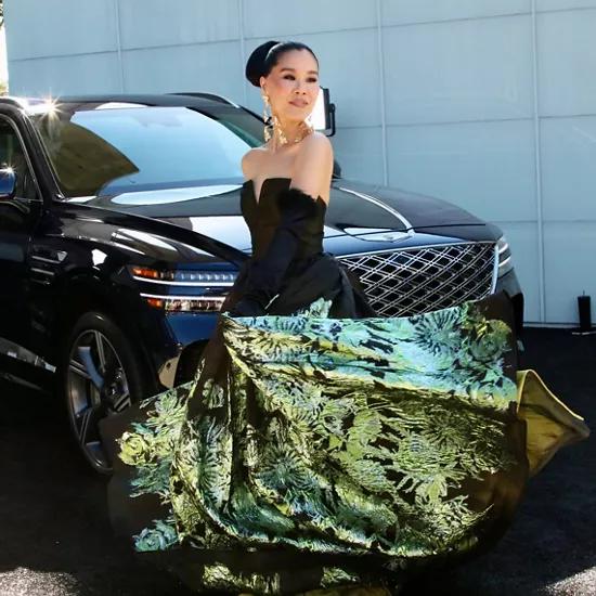 Woman in formal dress stands in front of Genesis SUV